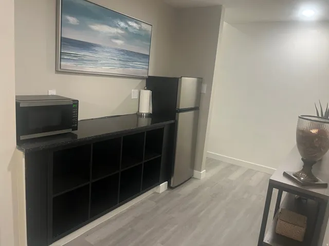 Compact kitchen area featuring a stainless steel refrigerator, built-in black cabinetry with open shelving, and wood-finish flooring