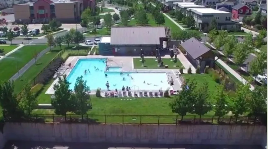 Outdoor pool area with surrounding green space, a community building, and paved walkways