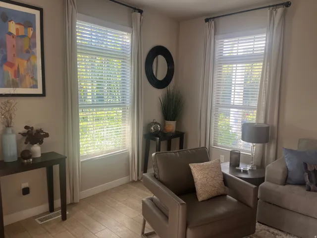 Two large windows with blinds, light-toned walls, and wood-finish flooring