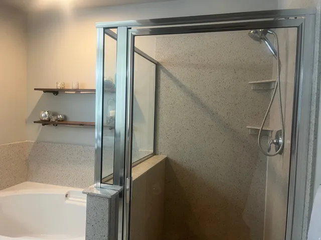 Glass-enclosed shower with a handheld shower fixture, built-in shelving, and speckled wall surround