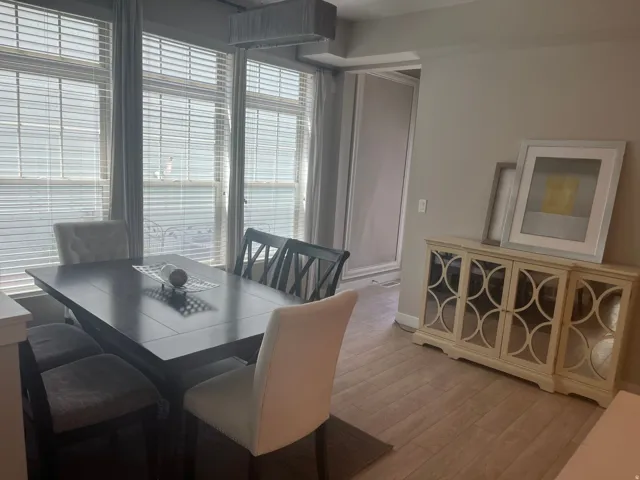 Expansive windows with horizontal blinds, recessed ceiling light fixture, wood-finish flooring, light-toned walls, and a decorative console cabinet with mirrored doors