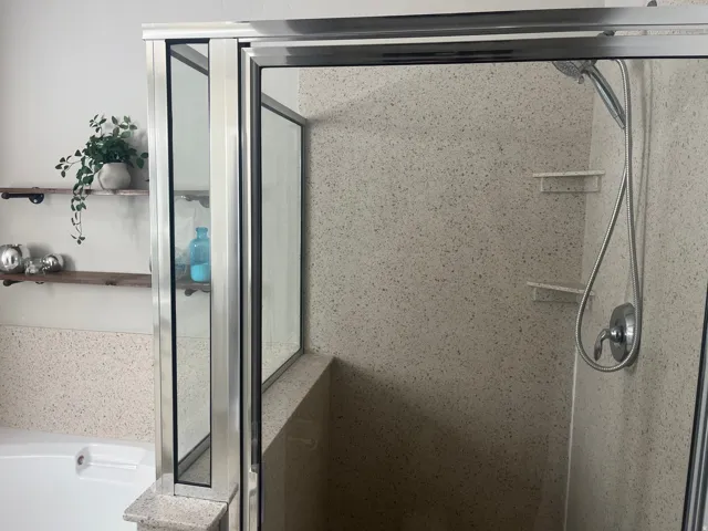 Glass-enclosed shower with a handheld showerhead, built-in shelving, and a built-in bench