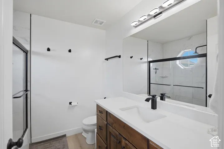 Spacious bathroom featuring a wood-finish vanity with an integrated sink, black hardware, a large mirror, a shower with a sliding glass door, and a shower window