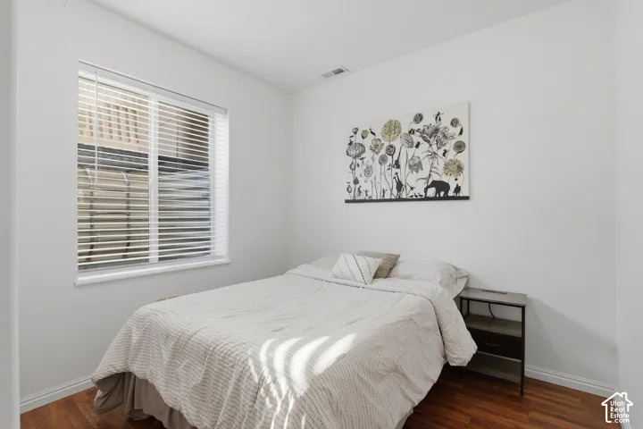 Wood-finish flooring with white baseboards, window with horizontal blinds, and white wall finishes