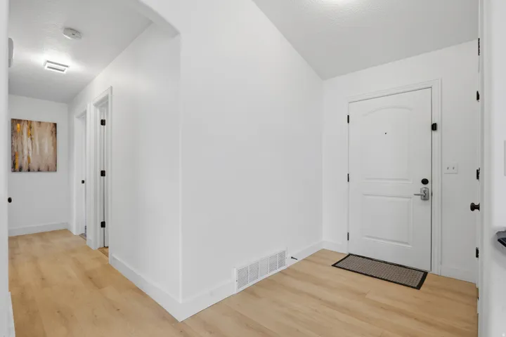 Entryway featuring wood-finish flooring, white paneled door with matte black hardware, and an arched doorway