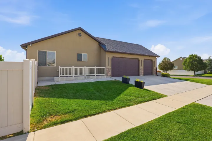Stucco exterior with stone accents, featuring a multi-car garage, concrete driveway, and a white privacy fence