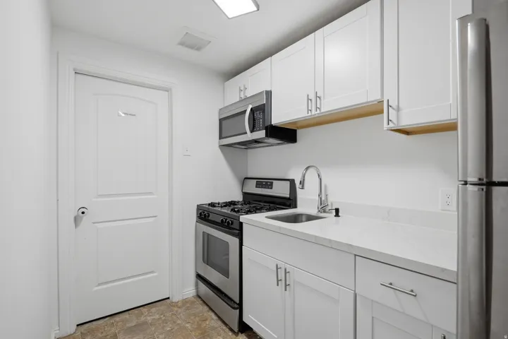 White shaker cabinetry with modern hardware, stainless steel appliances, light-toned countertops, and a stainless steel sink with a high-arc faucet