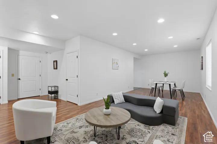 Recessed lighting illuminates the open-concept living space, featuring wood-finish flooring and a white color palette