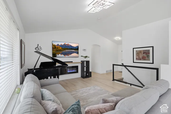Vaulted ceilings, wood-finish flooring, electric fireplace, modern ceiling fixture, and a black metal and glass railing