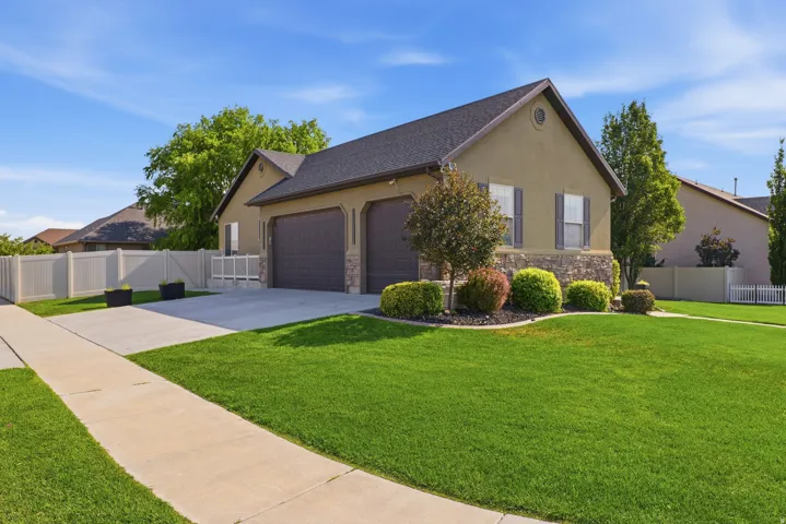 Stucco exterior with stone accenting, dark shingle roof, attached two-car garage, concrete driveway, and front lawn with mature landscaping