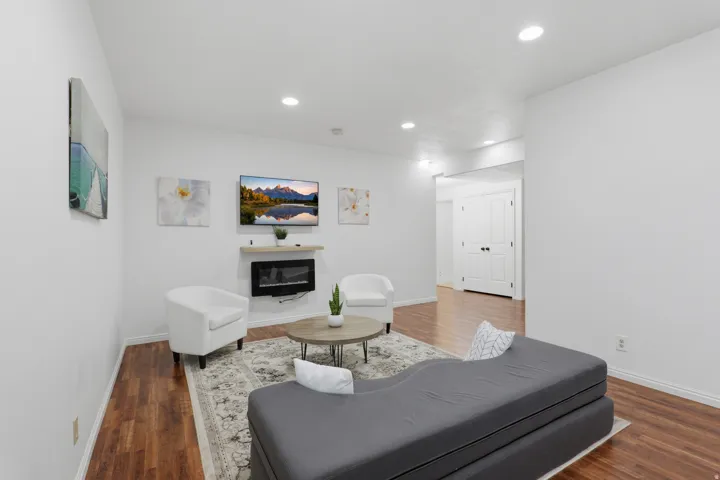 Recessed lighting, wood-finish flooring, white walls, built-in electric fireplace, and a floating wood-finish mantel