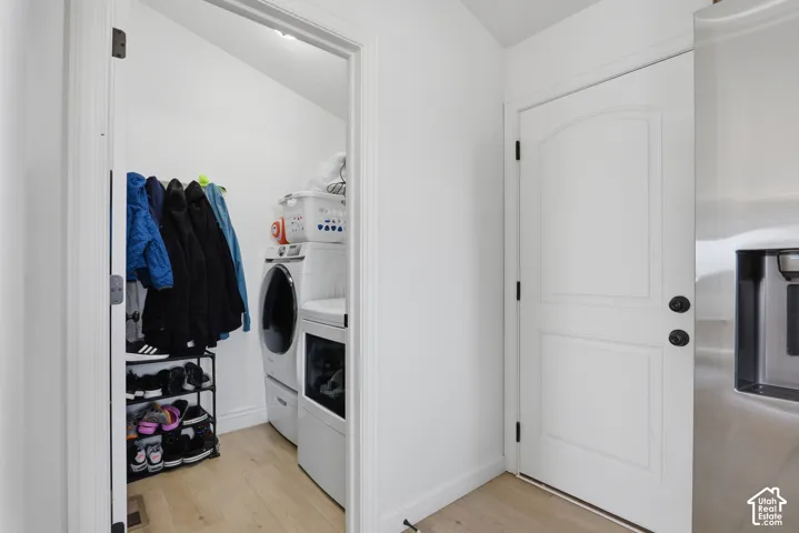 Recessed laundry area with stacked appliances, light wood-finish flooring, and a solid interior door with dark hardware