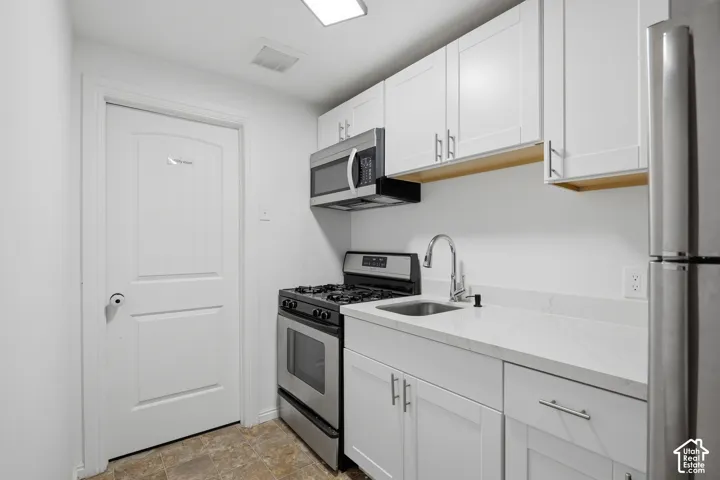 White shaker cabinetry with modern hardware, stainless steel appliances, light-toned countertops, and a stainless steel sink with a high-arc faucet