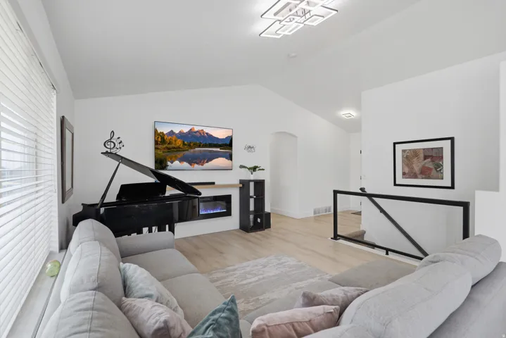 Vaulted ceilings, wood-finish flooring, electric fireplace, modern ceiling fixture, and a black metal and glass railing