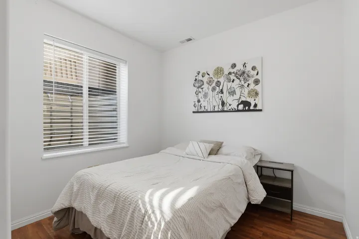 Wood-finish flooring with white baseboards, window with horizontal blinds, and white wall finishes
