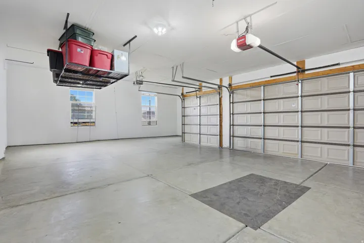 Spacious garage with concrete flooring, two paneled garage doors, overhead storage, and two windows providing natural light