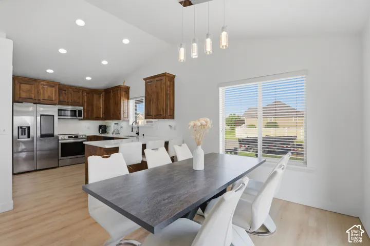 Vaulted ceilings with recessed lighting, wood-finish flooring, stainless steel appliances, kitchen island with counter seating, and a large window with horizontal blinds