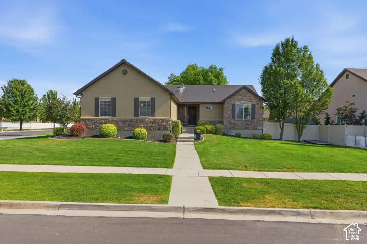 Stucco and stone exterior with dark shutters, gabled roofline, and established front landscaping
