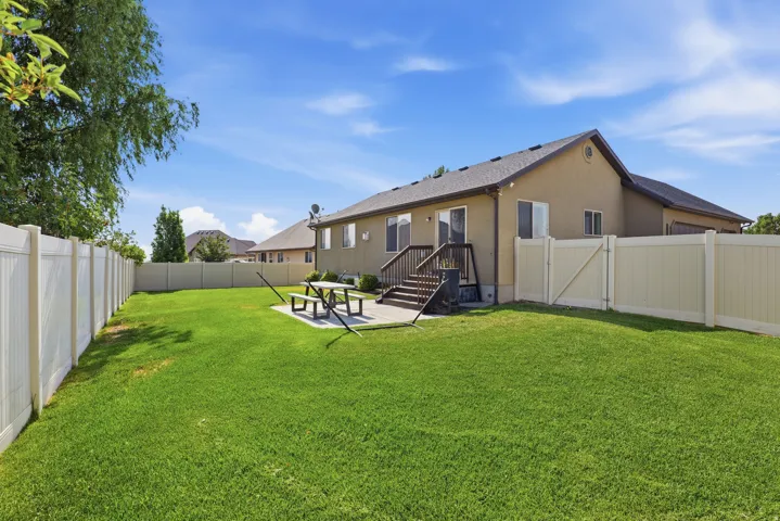 Expansive backyard featuring a manicured lawn, full privacy fencing, a concrete patio, and a wood deck with stairs