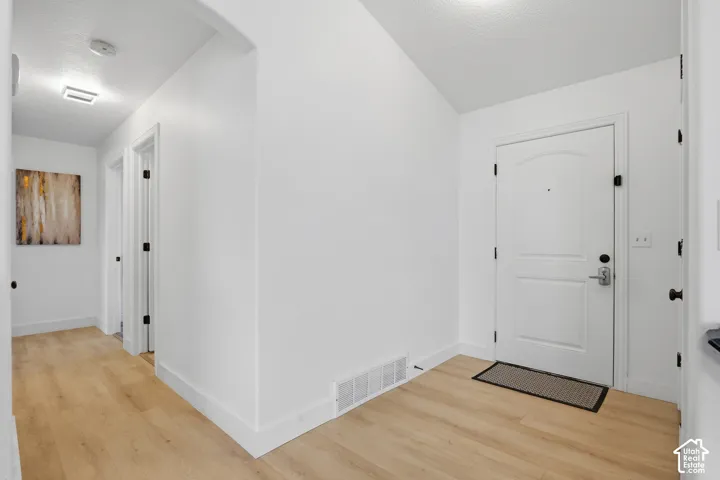 Entryway featuring wood-finish flooring, white paneled door with matte black hardware, and an arched doorway