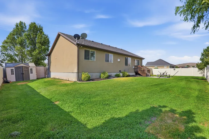 Expansive backyard featuring a manicured lawn, a privacy fence, a wooden deck, and a storage shed