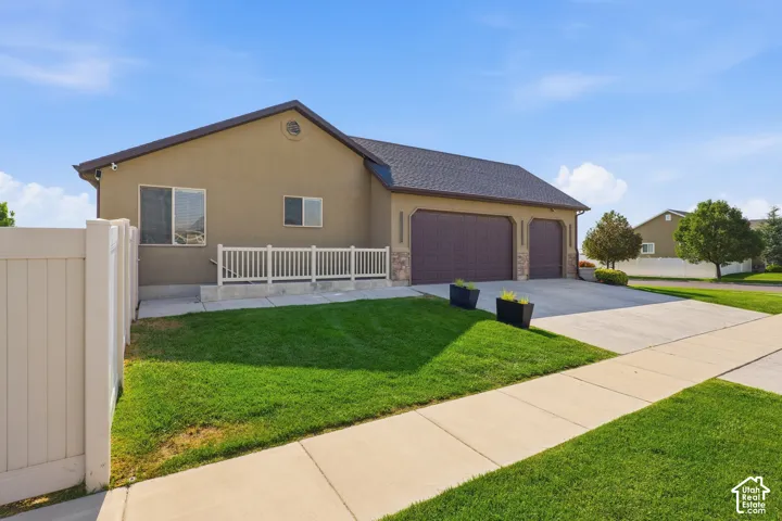 Stucco exterior with stone accents, featuring a multi-car garage, concrete driveway, and a white privacy fence
