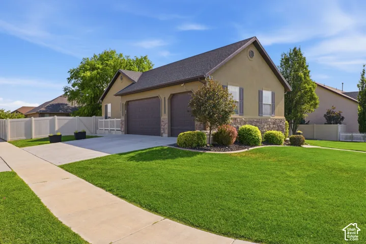 Stucco exterior with stone accenting, dark shingle roof, attached two-car garage, concrete driveway, and front lawn with mature landscaping