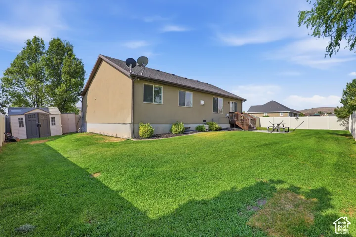 Expansive backyard featuring a manicured lawn, a privacy fence, a wooden deck, and a storage shed