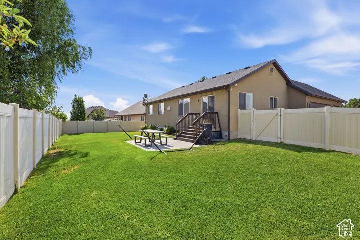 Expansive backyard featuring a manicured lawn, full privacy fencing, a concrete patio, and a wood deck with stairs