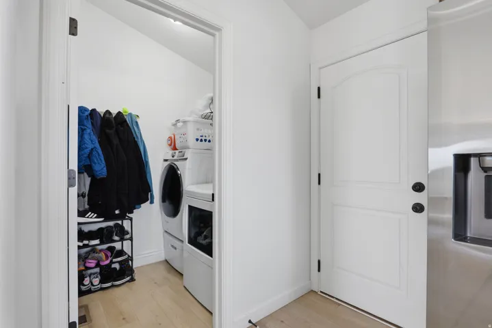 Recessed laundry area with stacked appliances, light wood-finish flooring, and a solid interior door with dark hardware