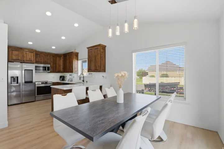 Vaulted ceilings with recessed lighting, wood-finish flooring, stainless steel appliances, kitchen island with counter seating, and a large window with horizontal blinds