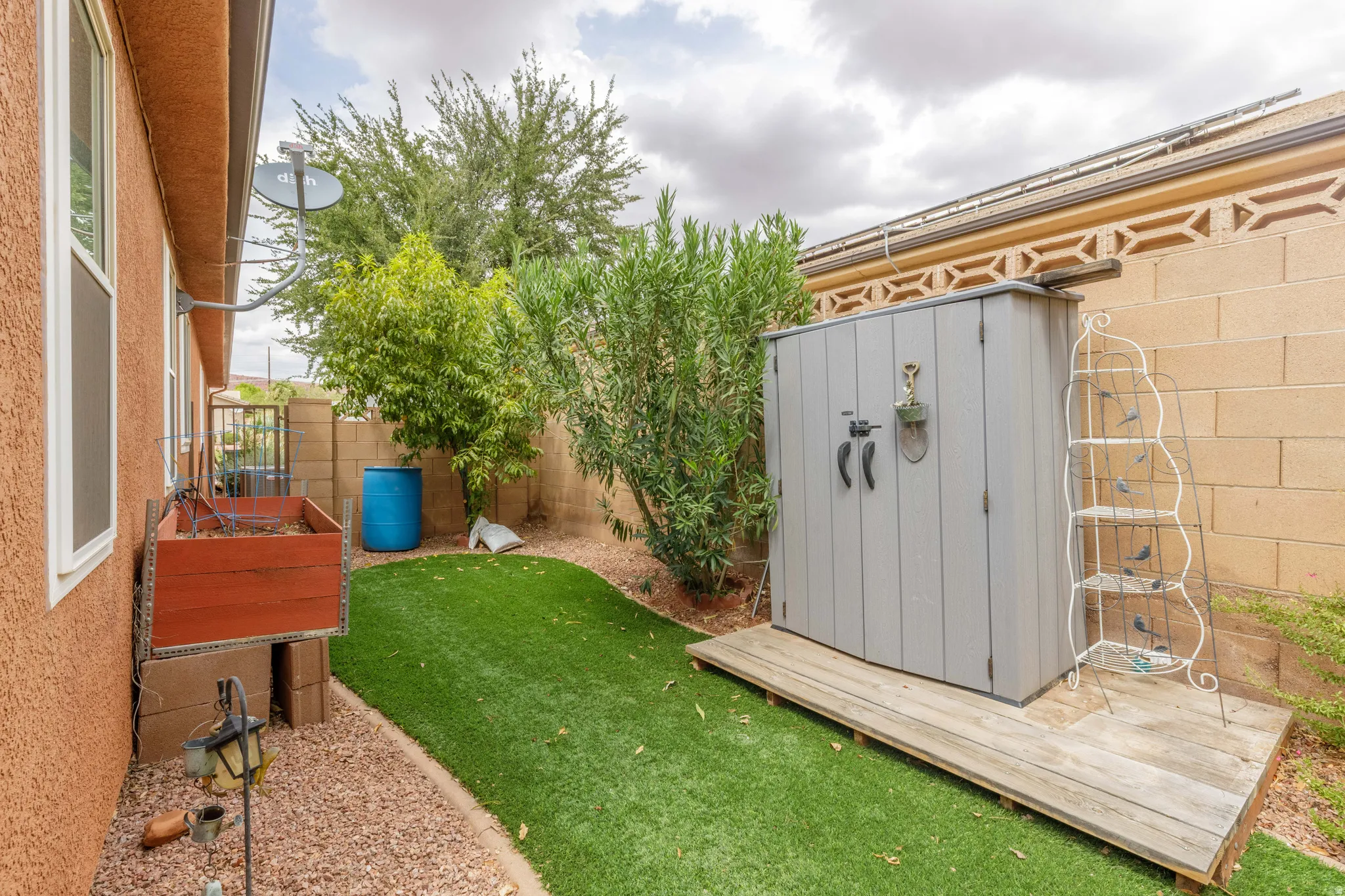 Enclosed backyard featuring artificial turf, gravel landscaping, a raised garden bed, and a storage shed on a wood platform