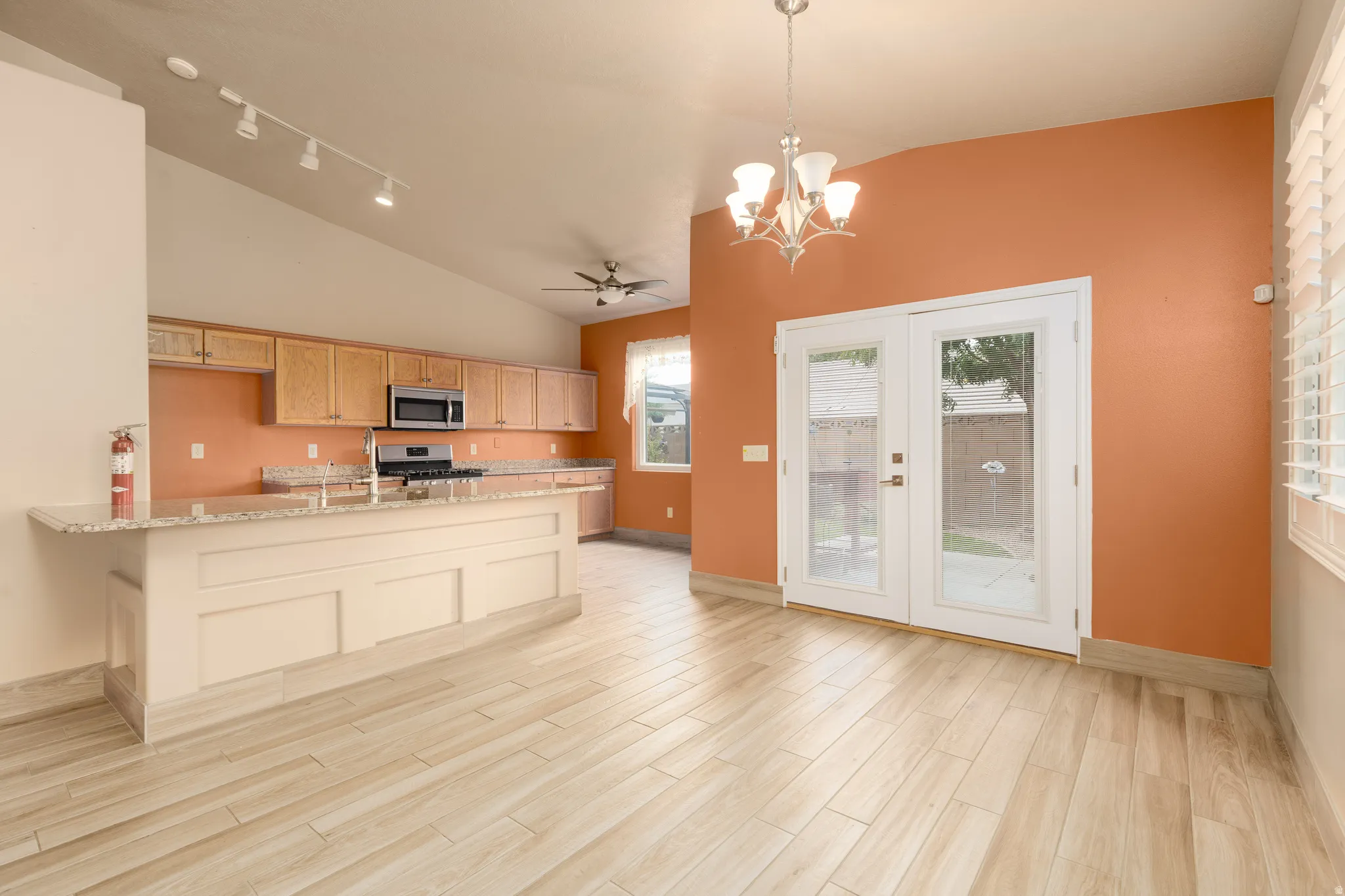 Vaulted ceilings, wood-look flooring, central island with an integrated sink, built-in microwave, and double glass-paneled doors