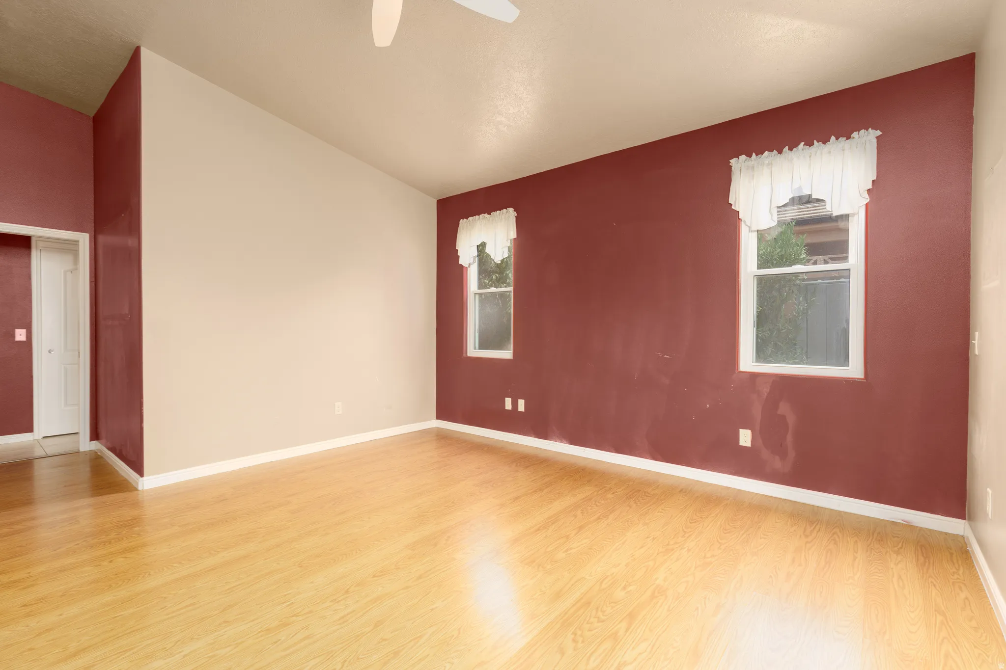 Vaulted ceiling room featuring wood-finish flooring, two windows, and a ceiling fan