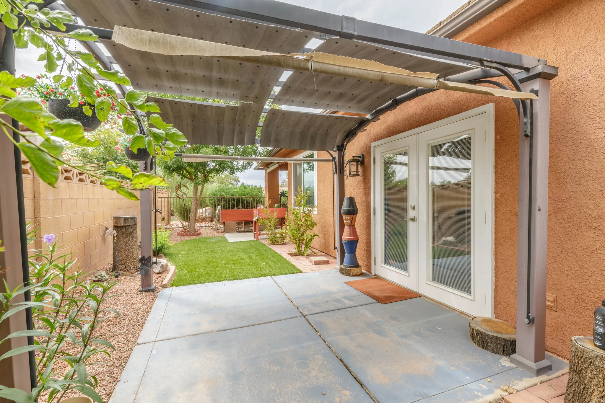 Patio area featuring a pergola with retractable shade, stucco exterior, double French doors, concrete patio, and a manicured lawn area