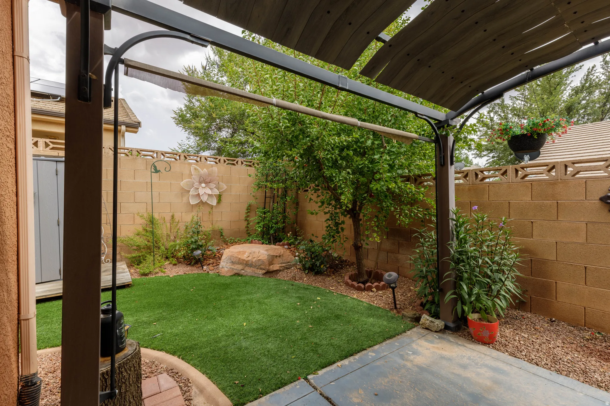 Patio area featuring a pergola with a slatted canopy, artificial turf, gravel accents, and a block wall perimeter