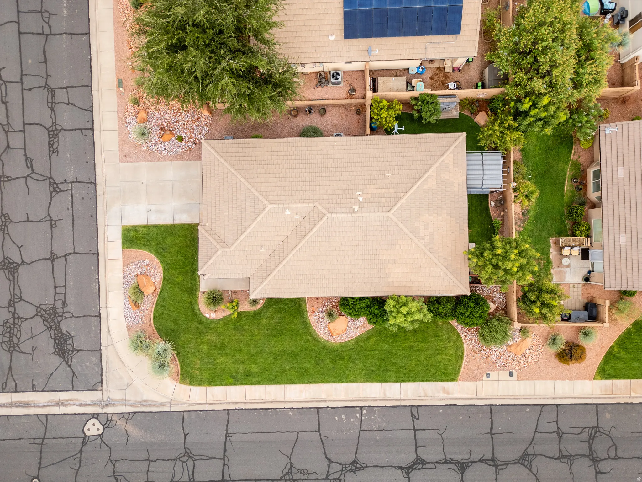 Pitched roof, front lawn with curved landscaping, desert-style landscaping with rocks and shrubs, paved driveway, mature trees
