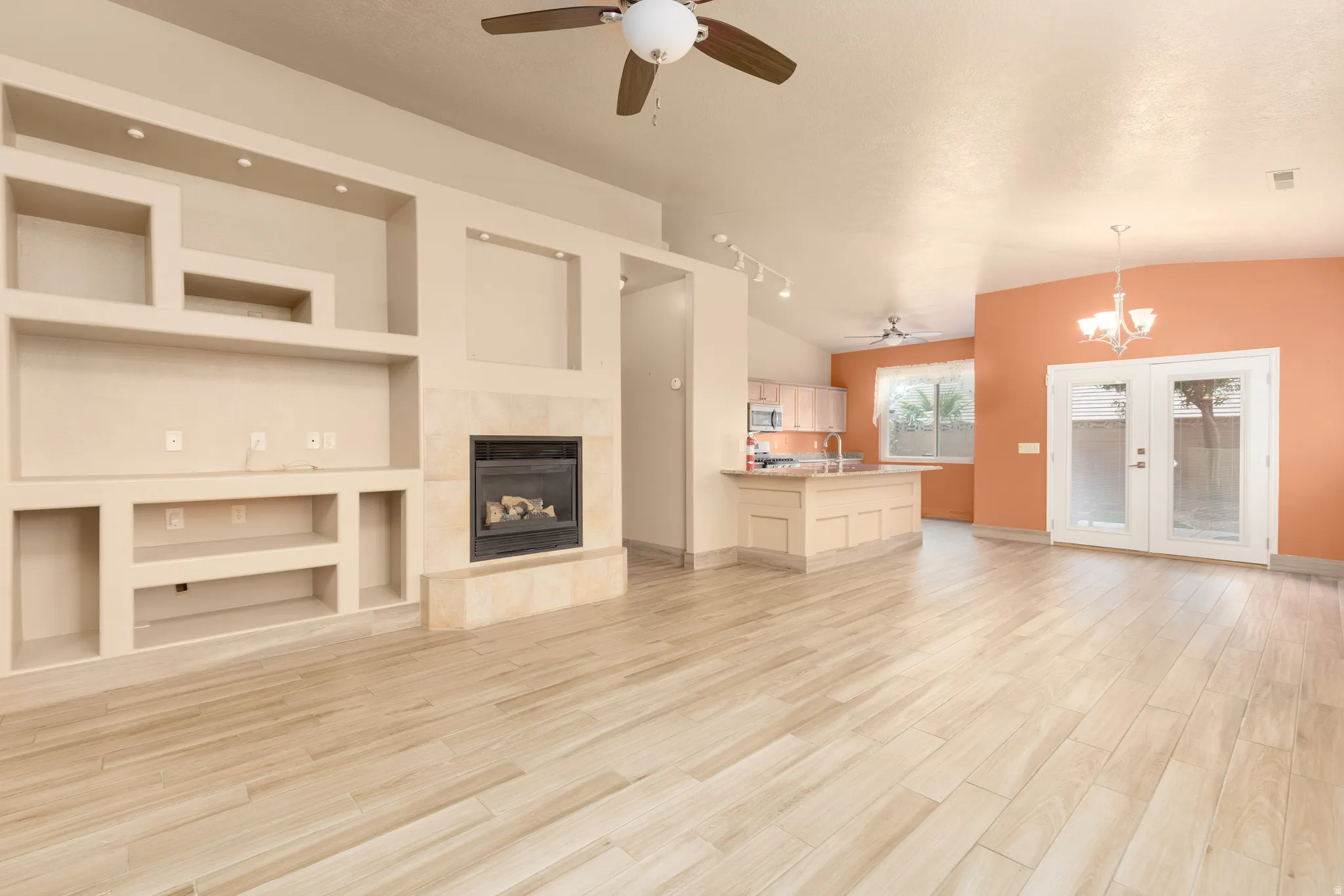 Recessed display shelving, built-in fireplace, vaulted ceiling, wood-finish flooring, and French doors