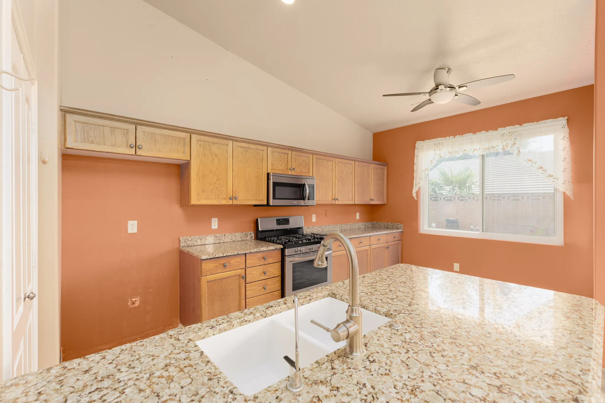 Kitchen featuring granite countertops, wood cabinetry, stainless steel appliances, and a vaulted ceiling