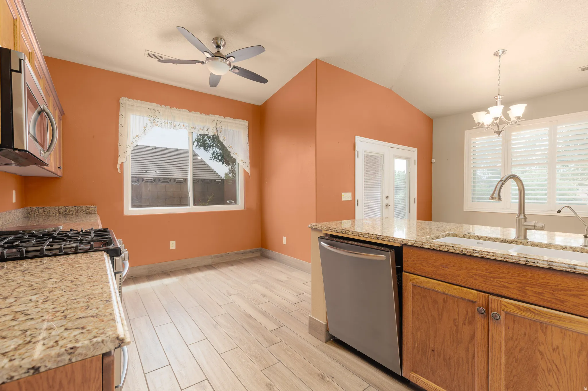 Kitchen featuring wood-finish flooring, granite countertops, stainless steel appliances, and a vaulted ceiling