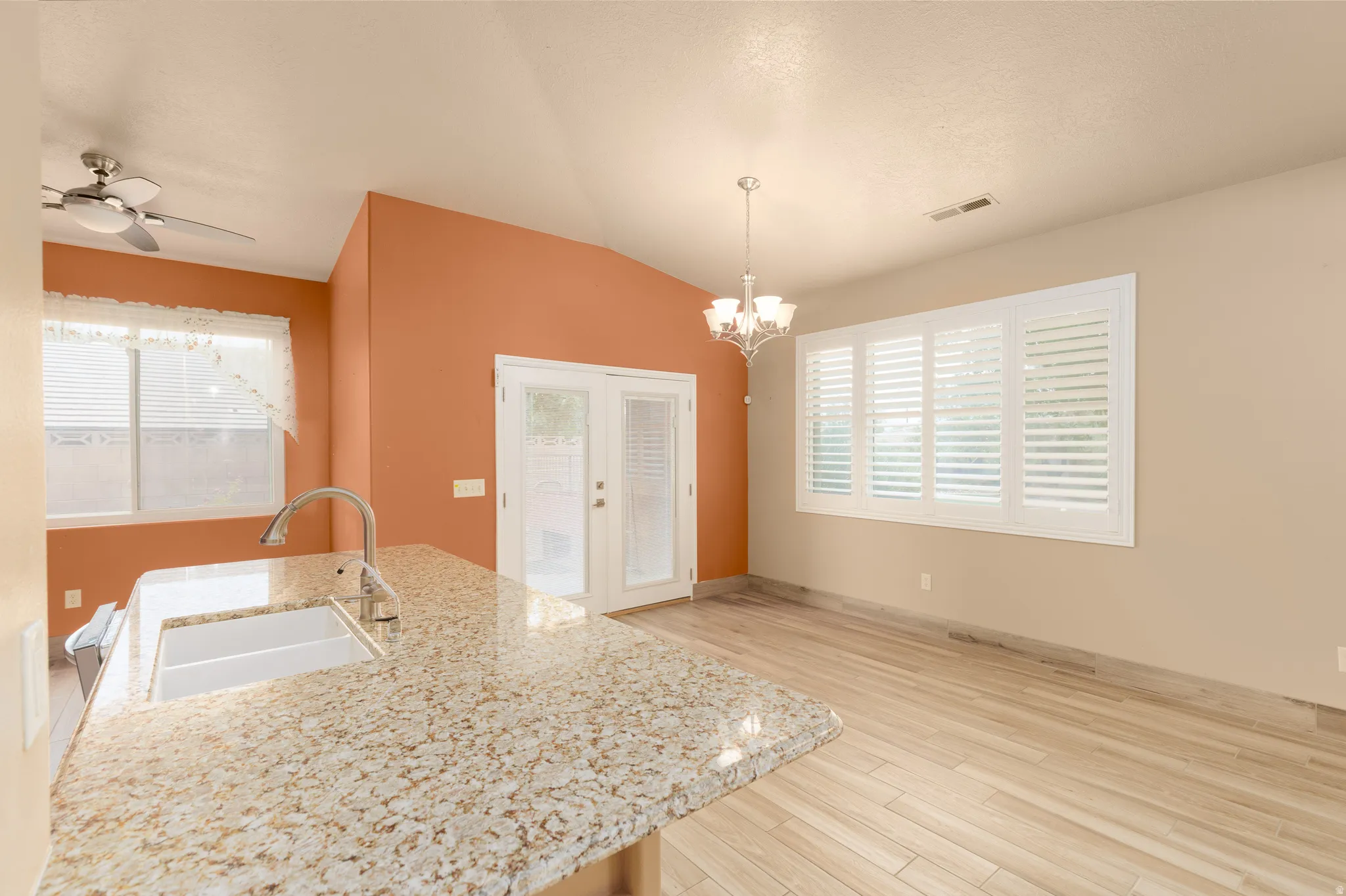 Angled ceiling, granite-look countertop, wood-finish flooring, plantation shutters, and French doors