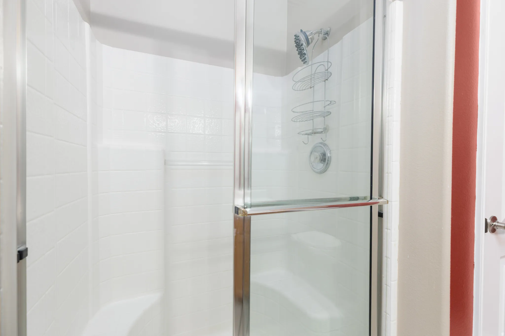 Shower enclosure with a clear glass sliding door, white tiled walls, and a built-in shower bench