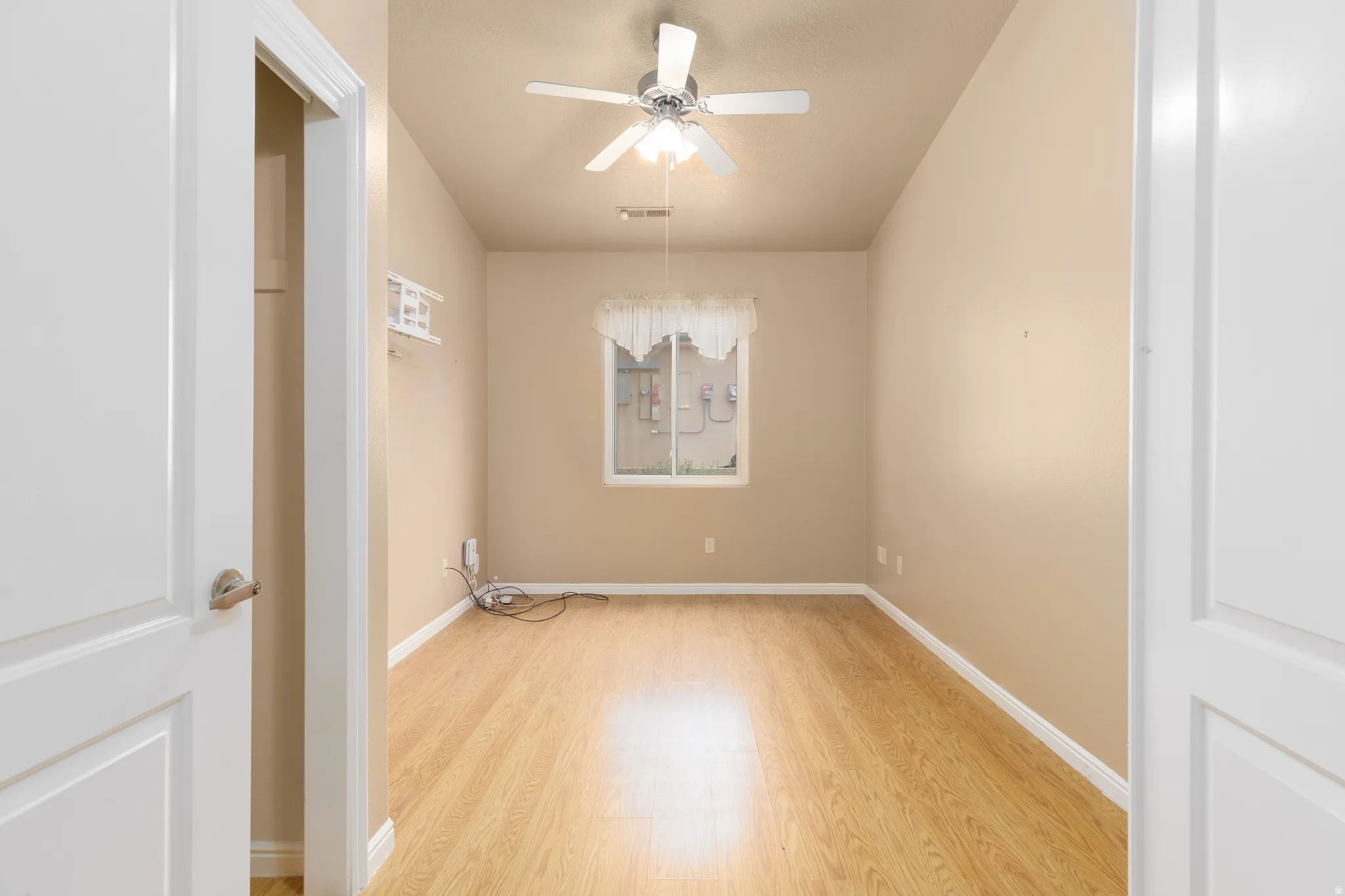 Wood-finish flooring, ceiling fan with integrated lighting, and a single window with white trim