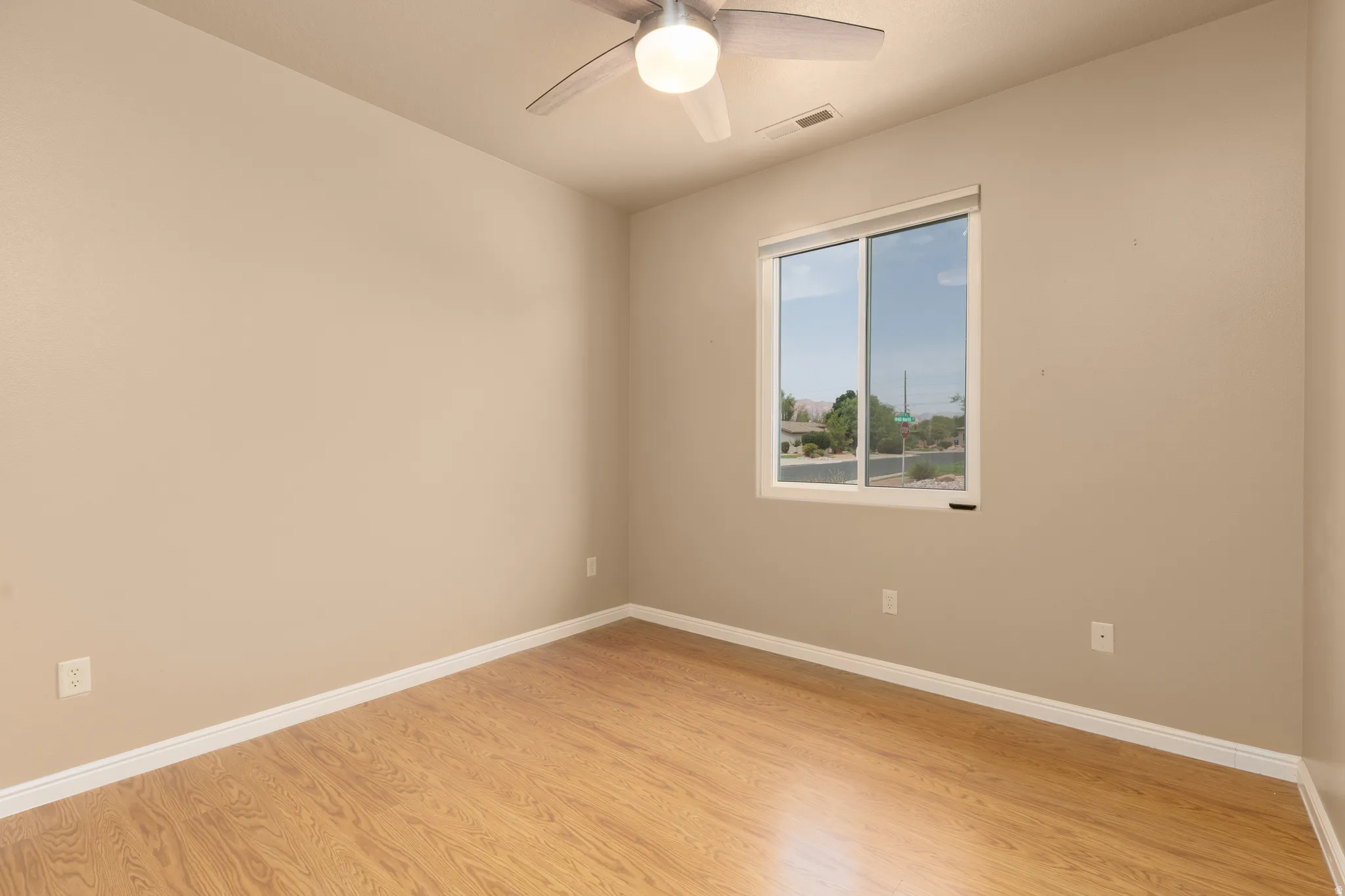 Light wood-finish flooring, neutral wall paint, white trim, a ceiling fan with integrated lighting, and a window with white framing