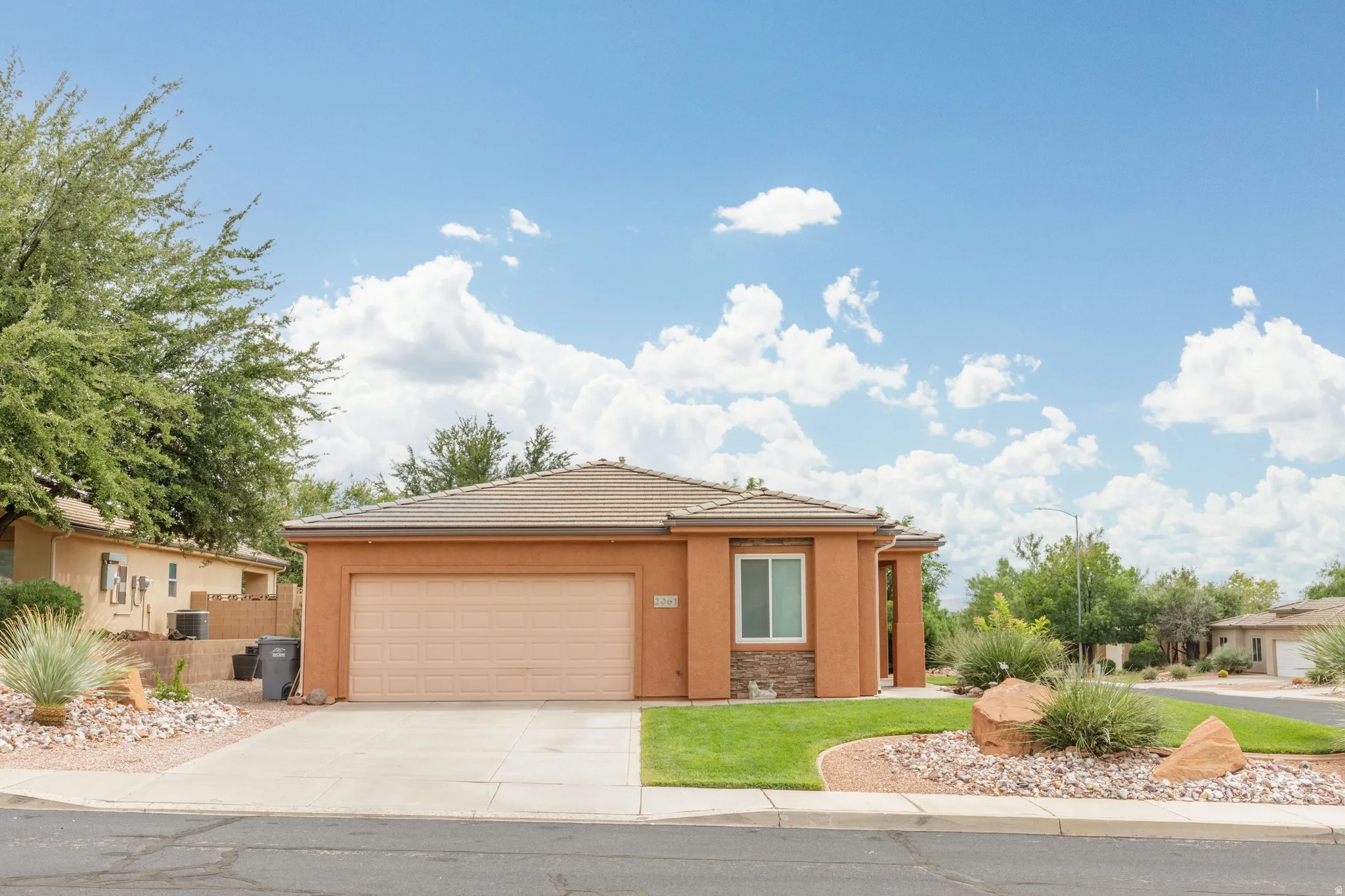 Single-story residence featuring a stucco exterior, attached garage, concrete driveway, and landscaped front yard with rock and shrub accents
