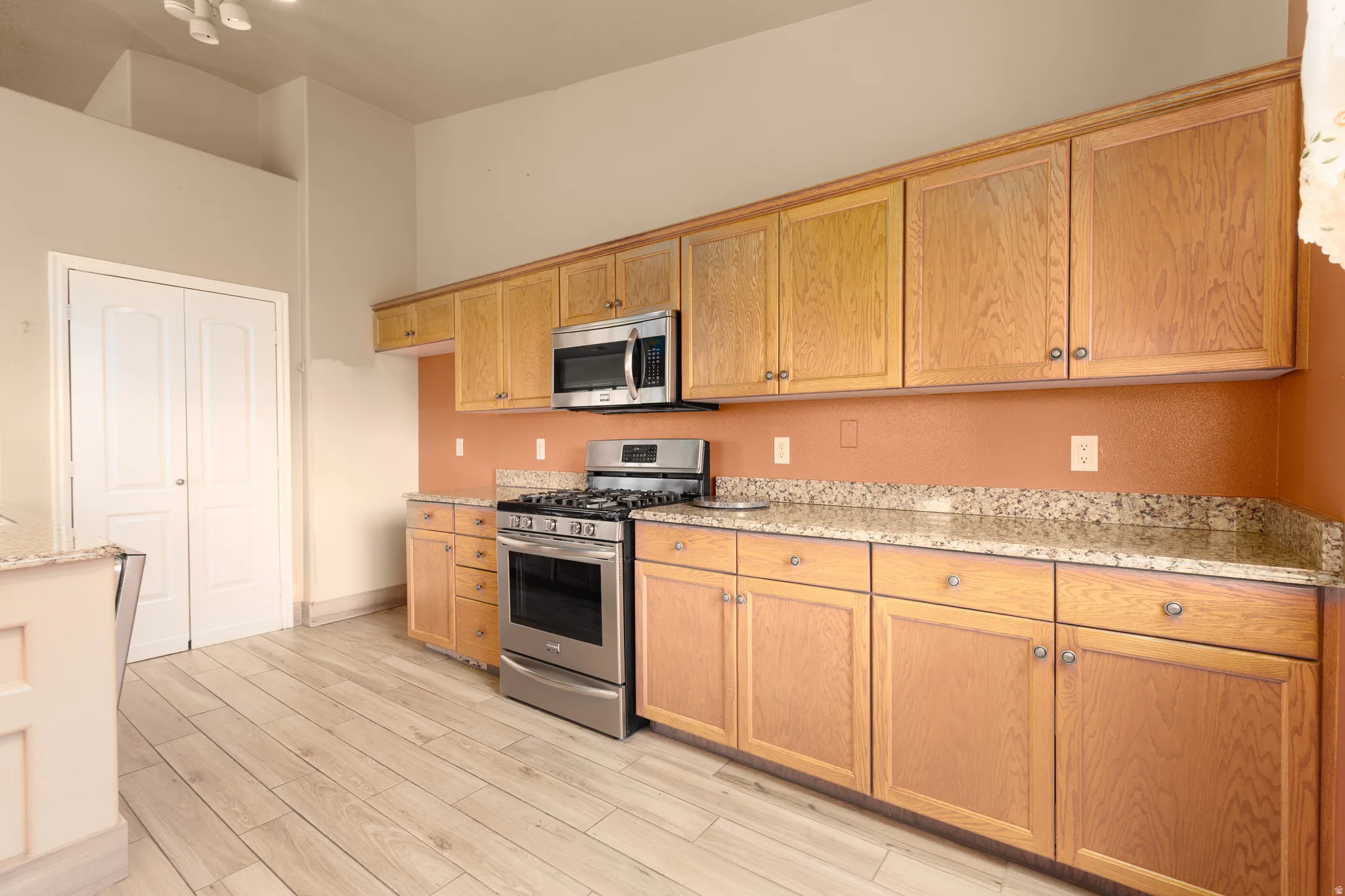 Kitchen featuring wood-finish cabinetry, stone countertops, and stainless steel appliances including a range and microwave