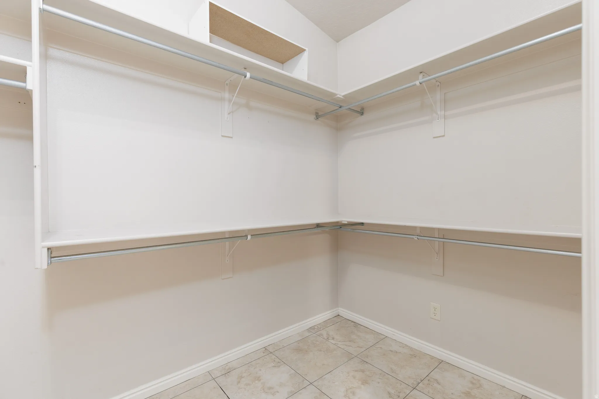 Walk-in closet featuring white shelving, chrome hanging rods, and neutral-toned tile flooring