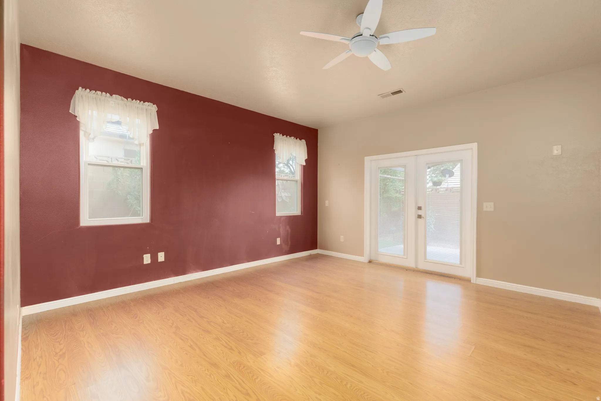Wood-finish flooring, dual windows with white trim, a ceiling fan, and French doors