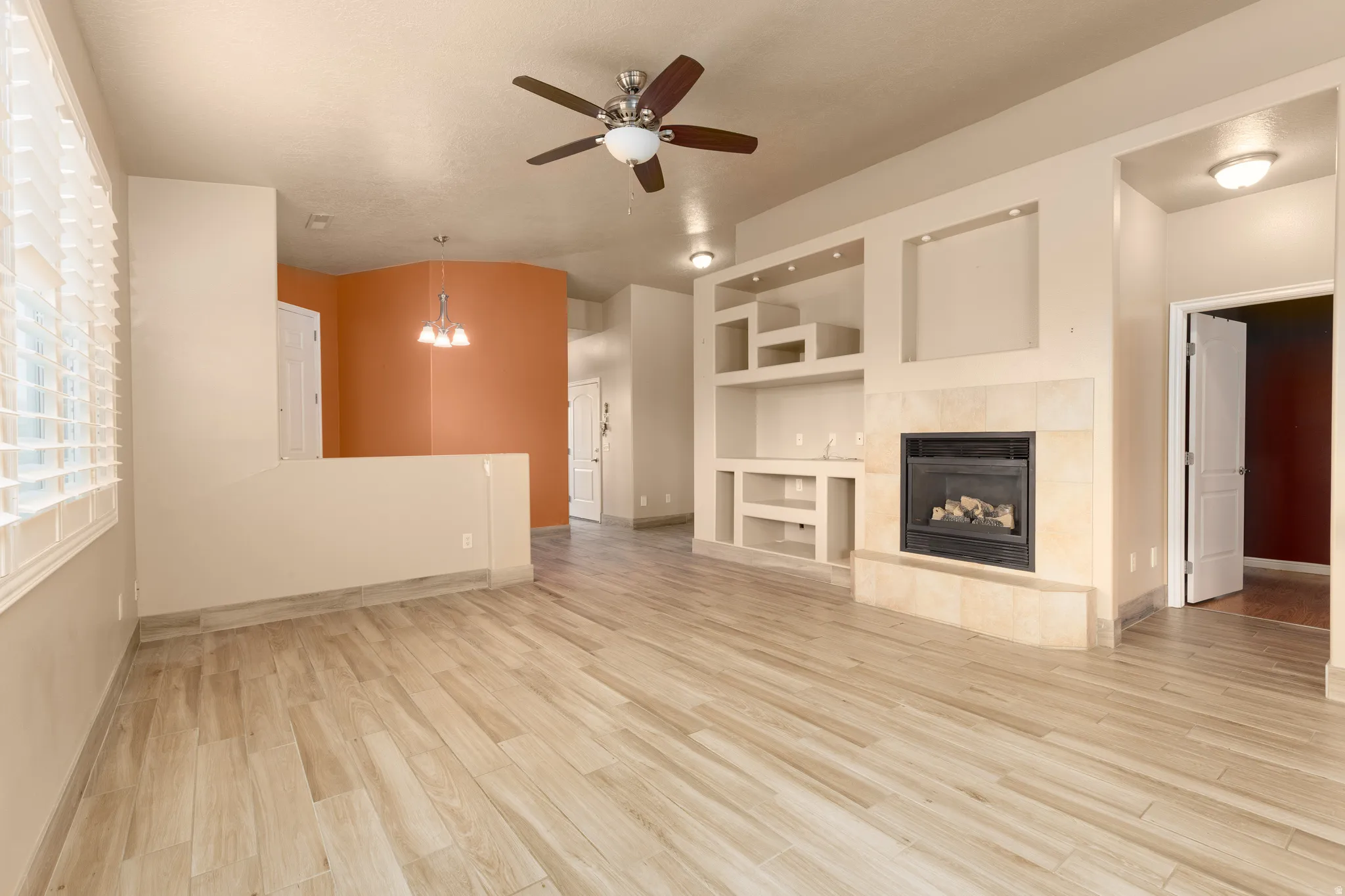 Wood-look tile flooring, built-in shelving, fireplace with stone surround, ceiling fan with integrated lighting, and window blinds