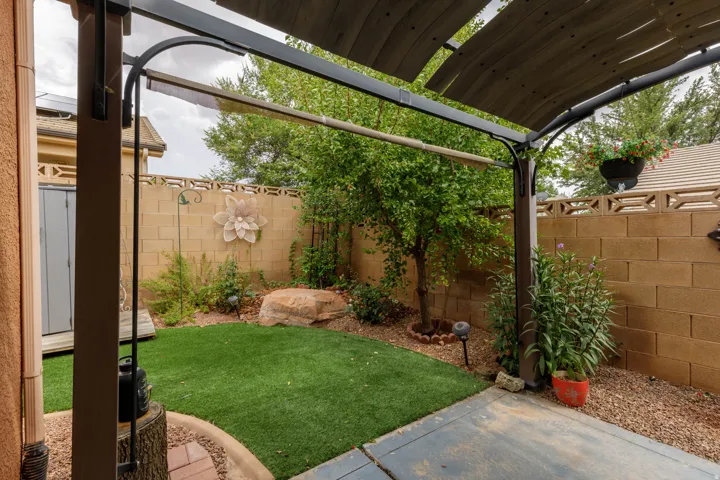 Patio area featuring a pergola with a slatted canopy, artificial turf, gravel accents, and a block wall perimeter